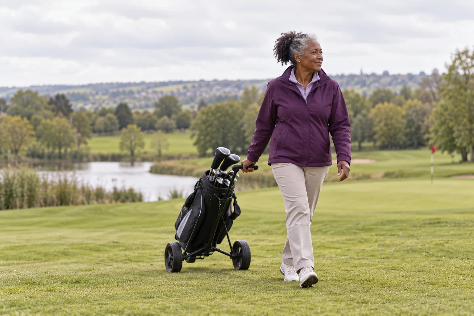 A woman pulling a golf trolley across a green